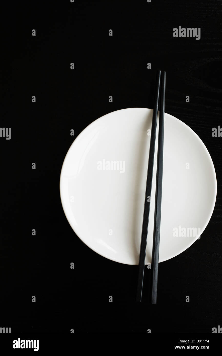 White plate with chopsticks on black background Stock Photo