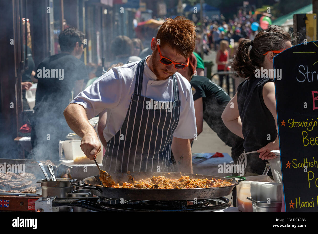 Chef cooking a pan of paella and and a grill of hamburgers on an