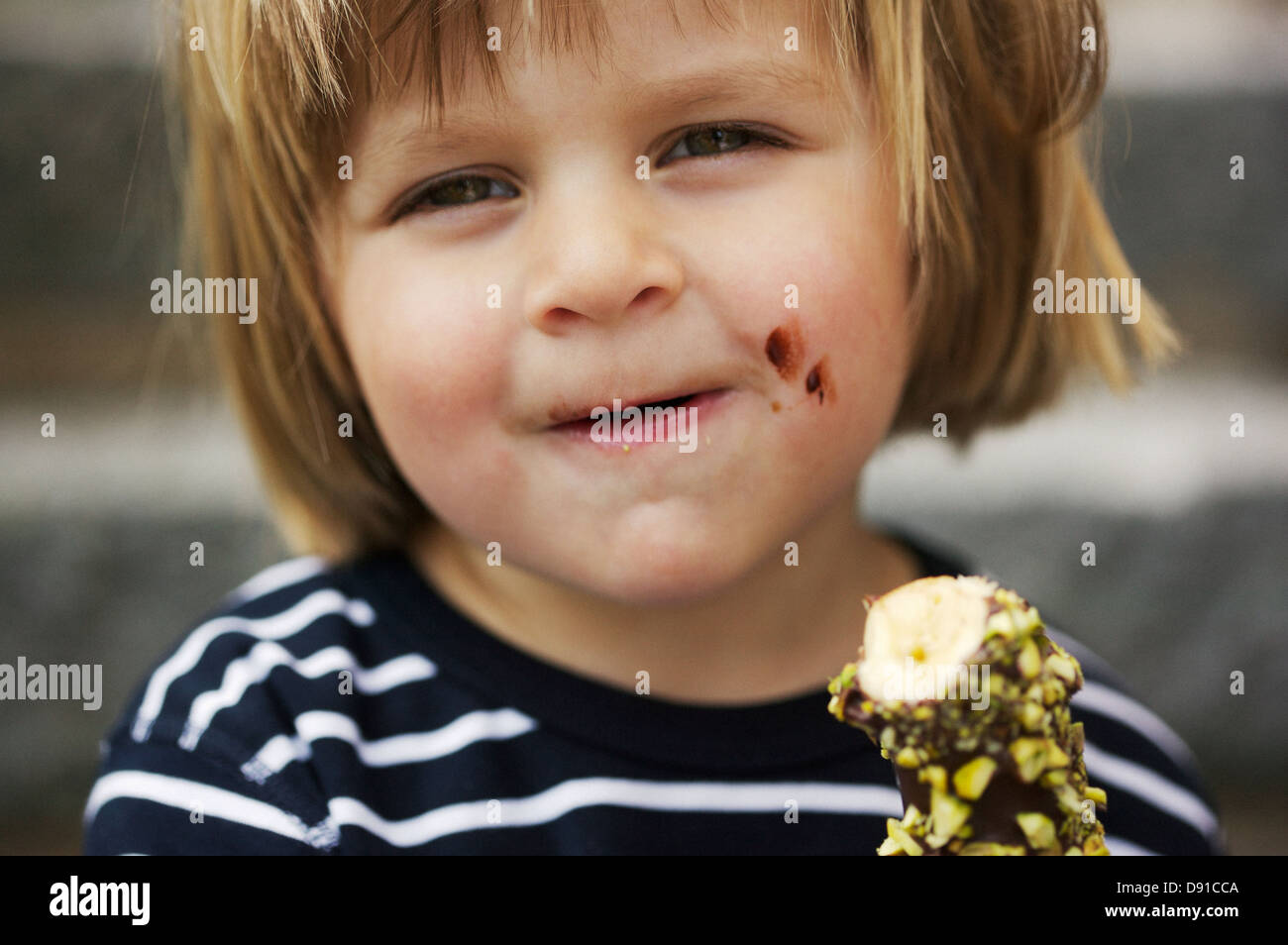 Boy eating a banana dipped in chocolate, Sweden. Stock Photo