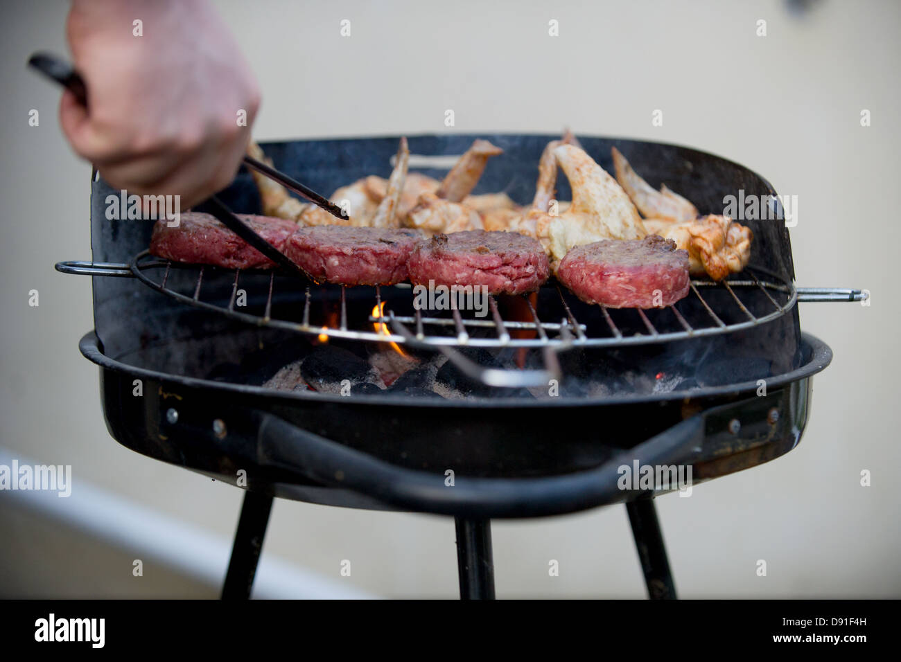 Beefburgers and chicken wings cooking on a barbeque in a British garden. Stock Photo