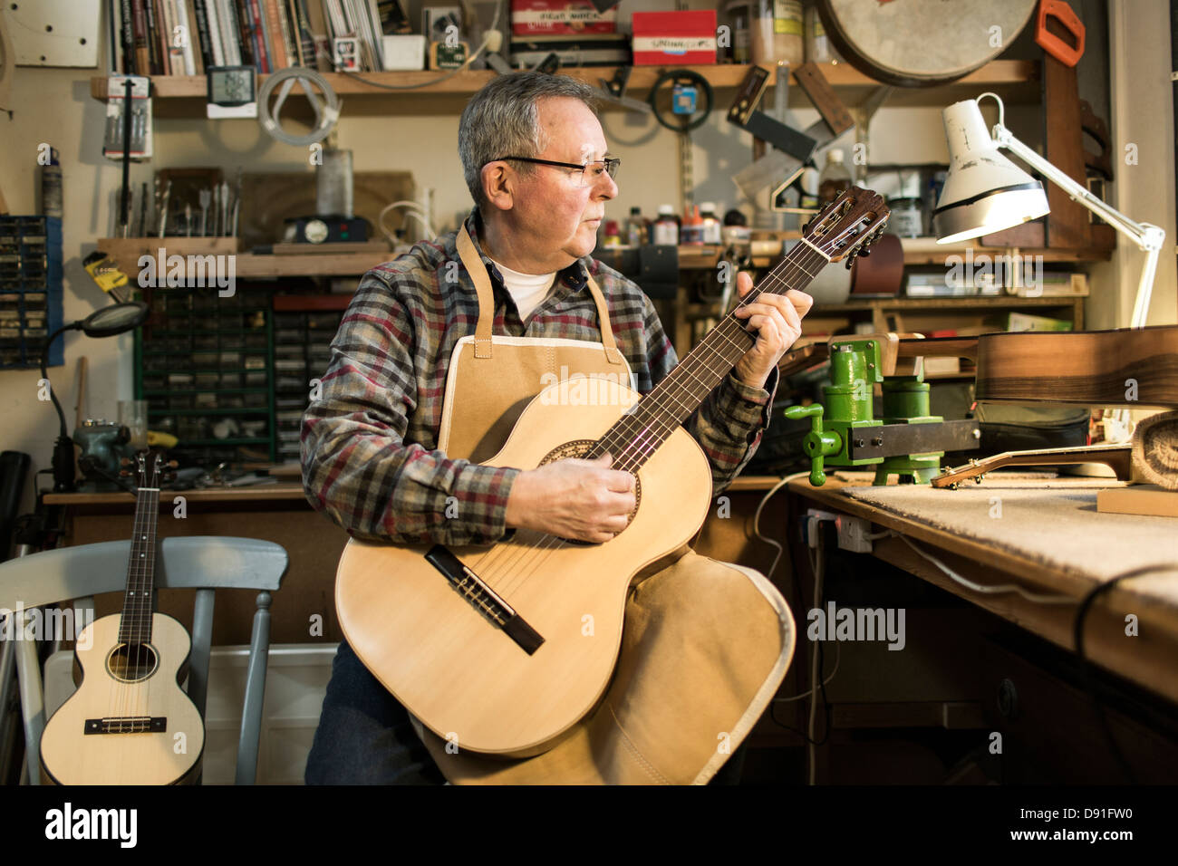 Guitar maker tuning and testing acoustic guitar in Stock Photo