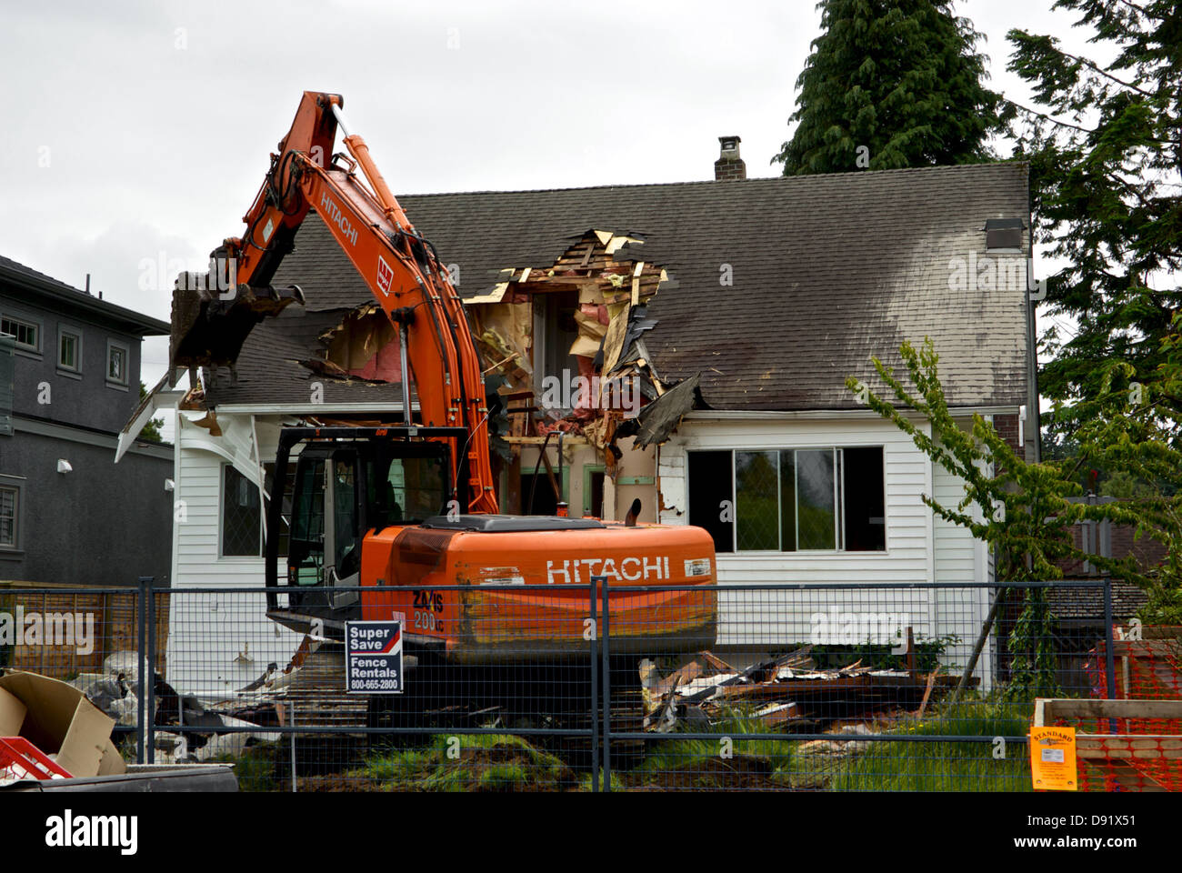 Hitachi Zaxix 200 LC excavator operator using hydraulic arm clamshell bucket to demolish roof old Vancouver house redevelopment Stock Photo