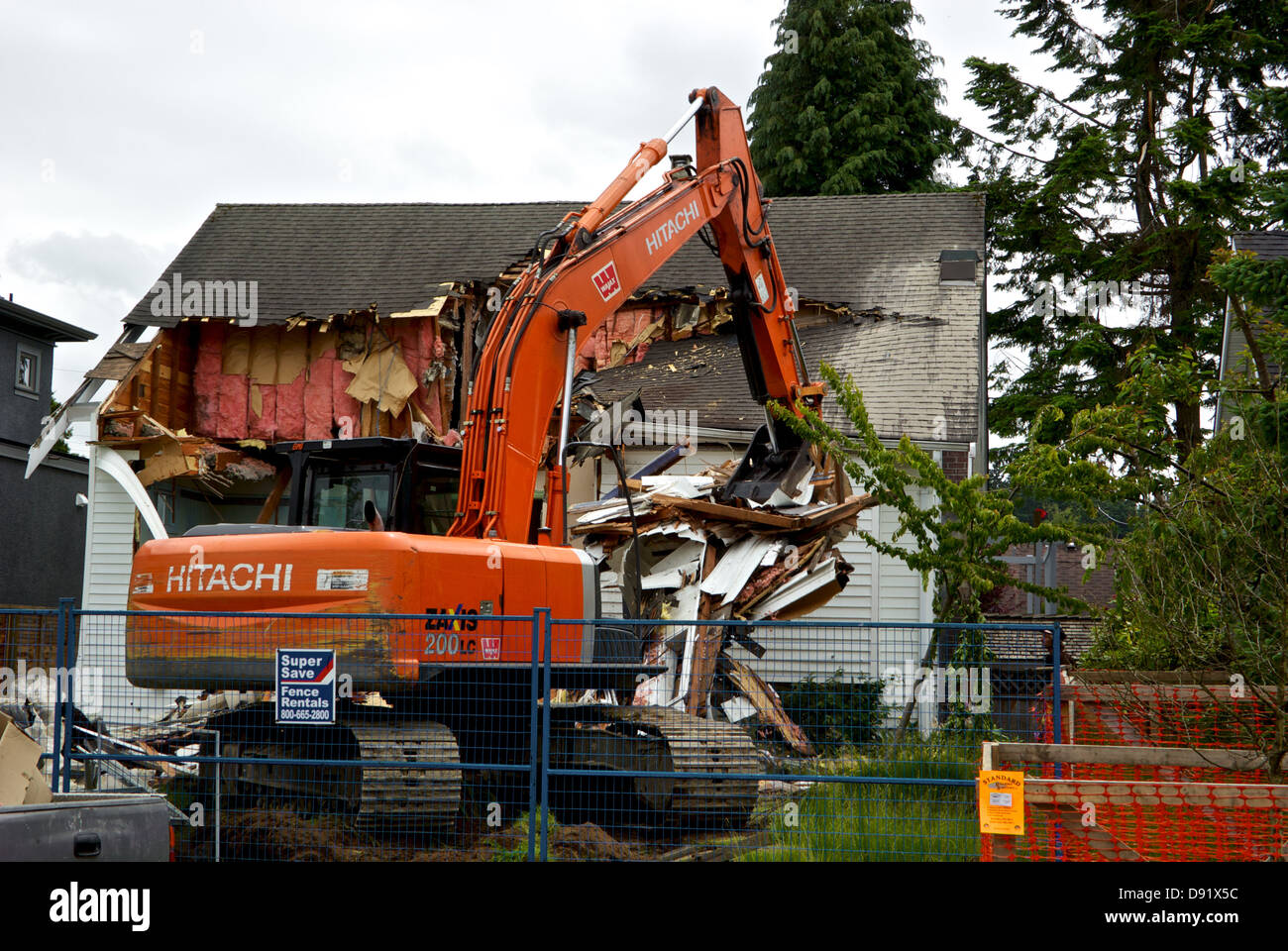 Hitachi Zaxix 200 LC excavator operator using hydraulic arm clamshell bucket to demolish roof old Vancouver house redevelopment Stock Photo
