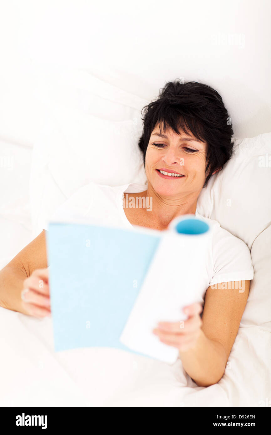 beautiful mature woman reading book on bed at home Stock Photo