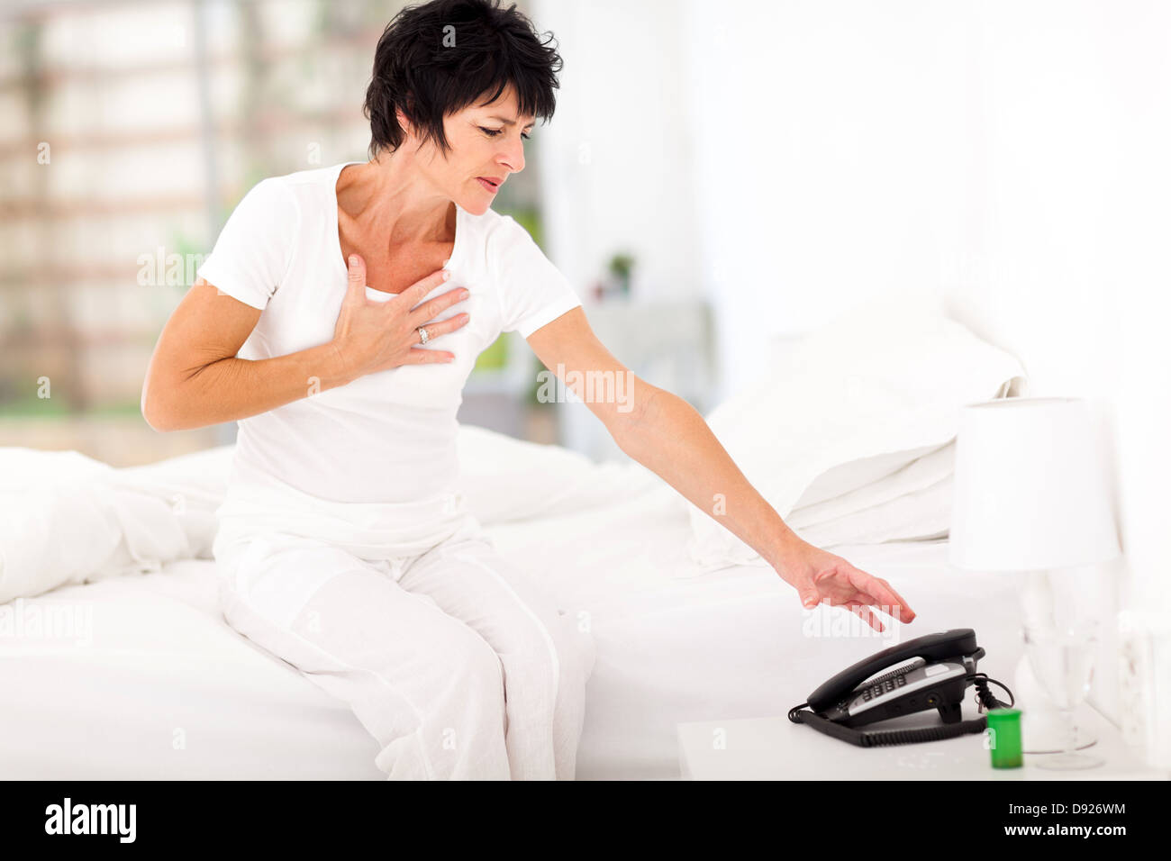 middle aged woman having heart attack and trying to reach telephone for help Stock Photo