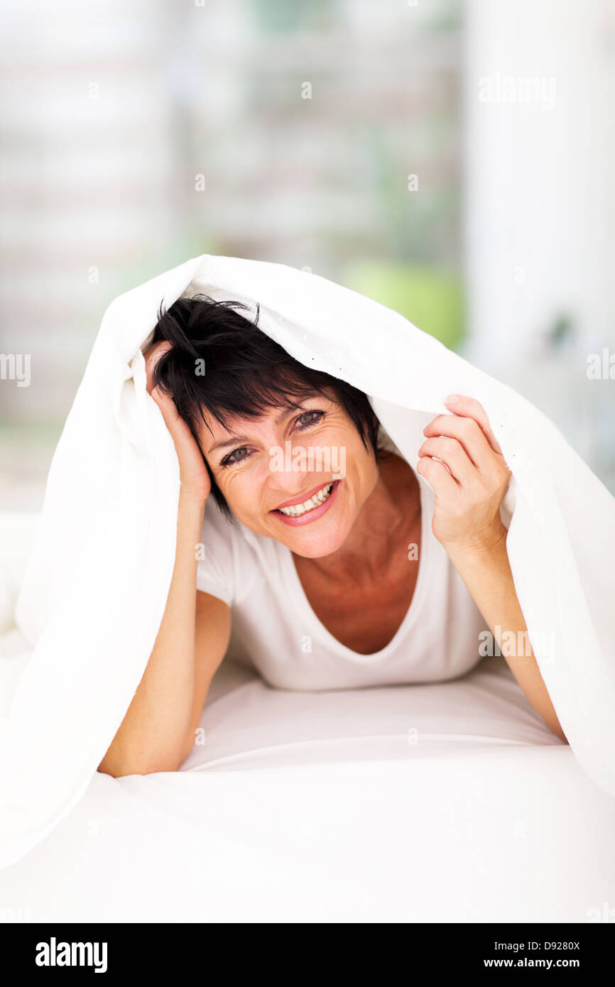 fun middle aged woman lying under duvet laughing Stock Photo