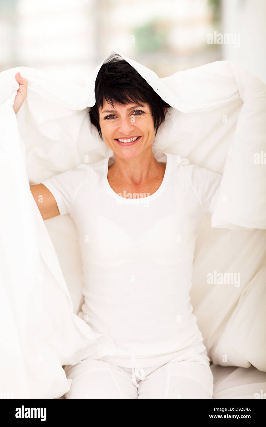 happy middle aged woman having fun with duvet in bedroom Stock Photo