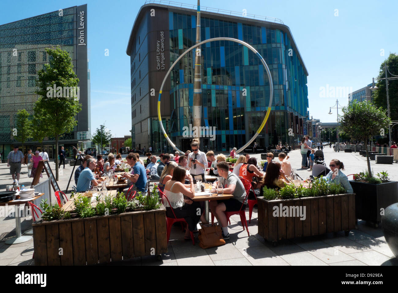 People sitting at tables outside in the street at Jamie's Italian Restaurant near John Lewis store and Cardiff Central Library Wales UK  KATHY DEWITT Stock Photo