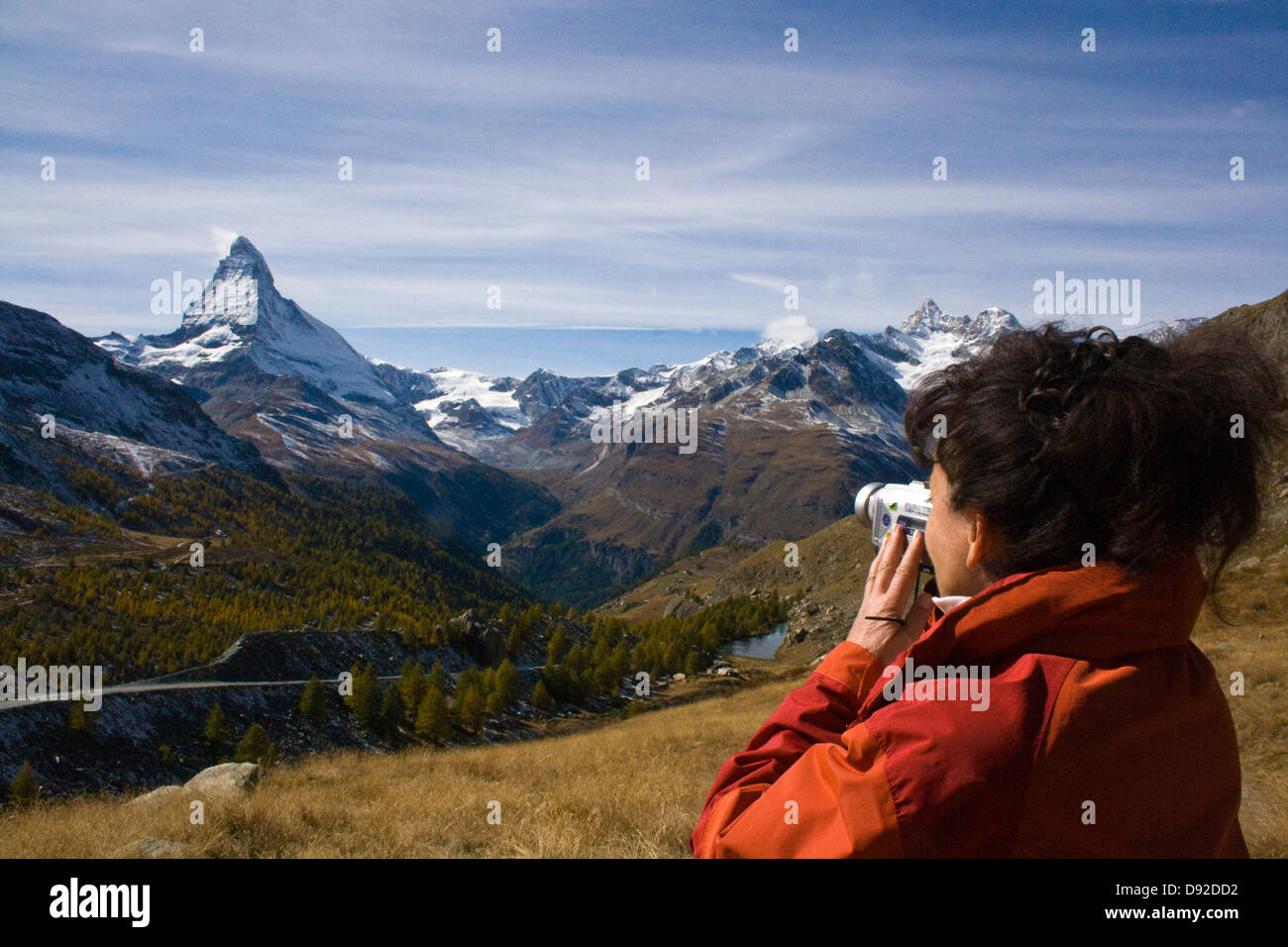 Woman in red jacket taking a picture of Matterhorn- Frau in roter Jacke richtet ihre Video-Kamera auf das Matterhorn Stock Photo