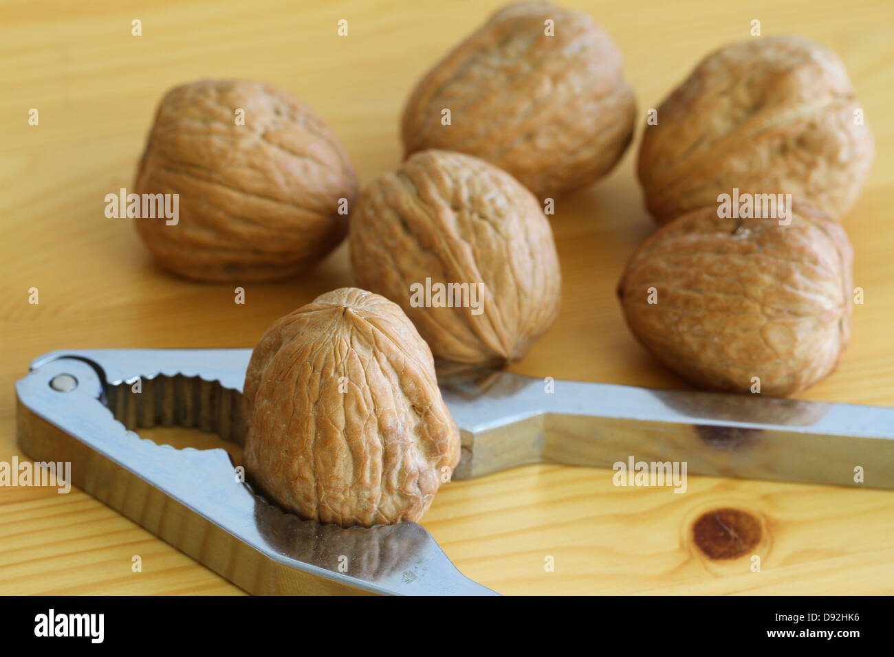 Whole walnuts and nut cracker on wood surface Stock Photo