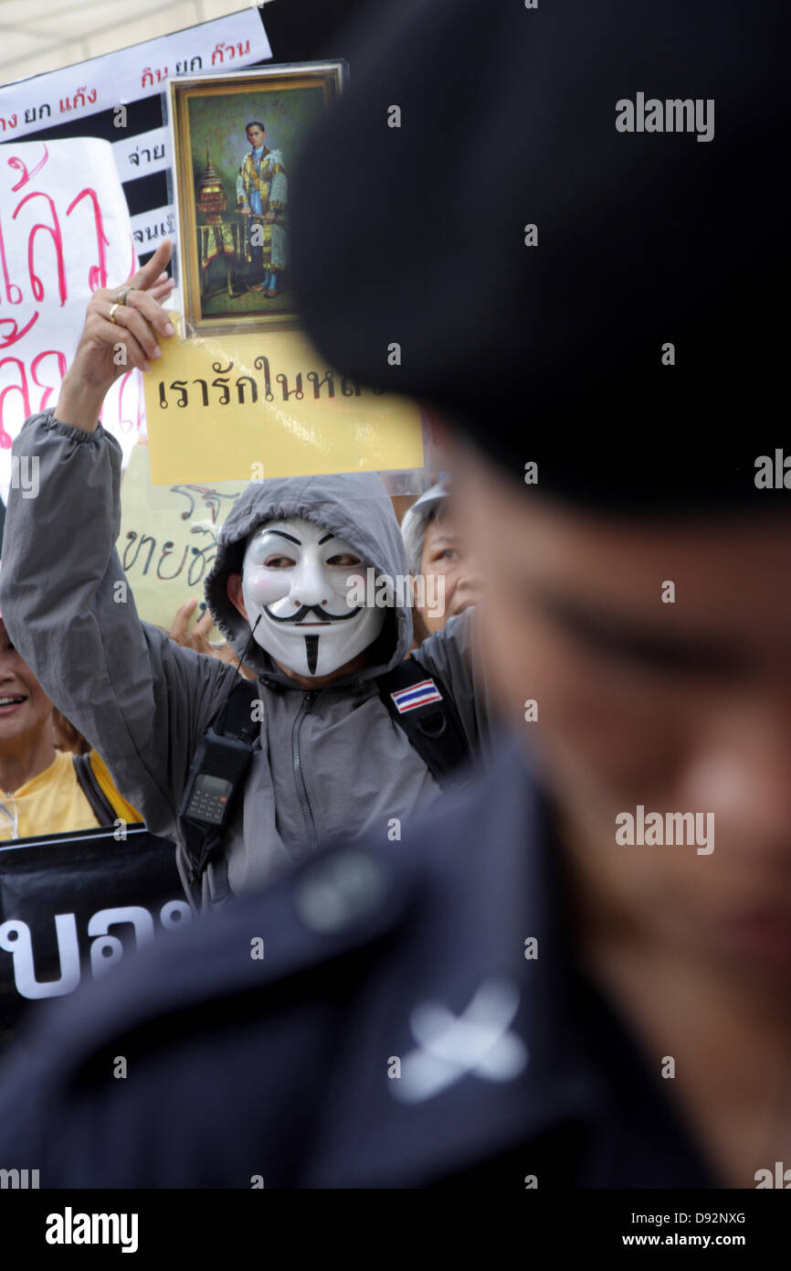 Bangkok , Thailand. 9th June 2013. Guy Falkes white mask protesters during protest behind a riot policeman at The Bangkok Art and Culture Centre. Protesters wearing "Guy Fawkes" continue to rally in Bangkok and others parts of Thailand against the Yingluck Shinawatra government, which opponents say is a "puppet" regime controlled by fugitive former premier Thaksin Shinawatra. Credit:  John Vincent/17�Թ����� Live News Stock Photo