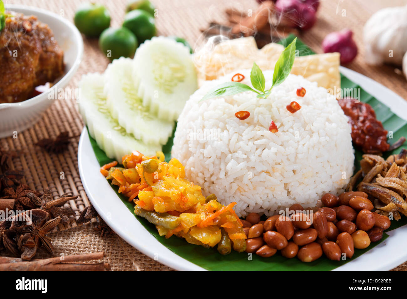 Nasi lemak kukus traditional malaysian spicy rice dish, fresh cooked with hot steam. Served with belacan, ikan bilis, acar, peanuts and cucumber. Decoration setup. Stock Photo