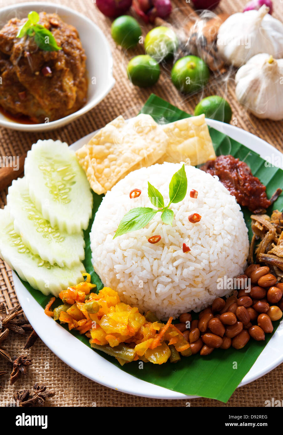 Nasi lemak traditional malaysian spicy rice dish, fresh cooked with hot steam. Served with belacan, ikan bilis, acar, peanuts and cucumber. Decoration setup. Stock Photo