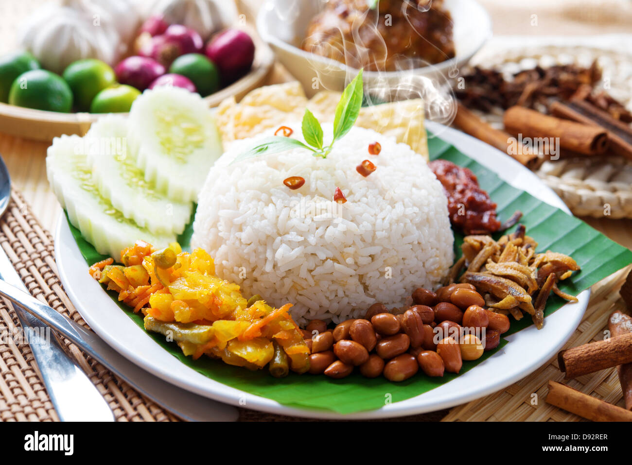 Nasi lemak traditional malaysian hot and spicy rice dish, fresh cooked with hot steam. Served with belacan, ikan bilis, acar, peanuts and cucumber. Decoration setup. Stock Photo