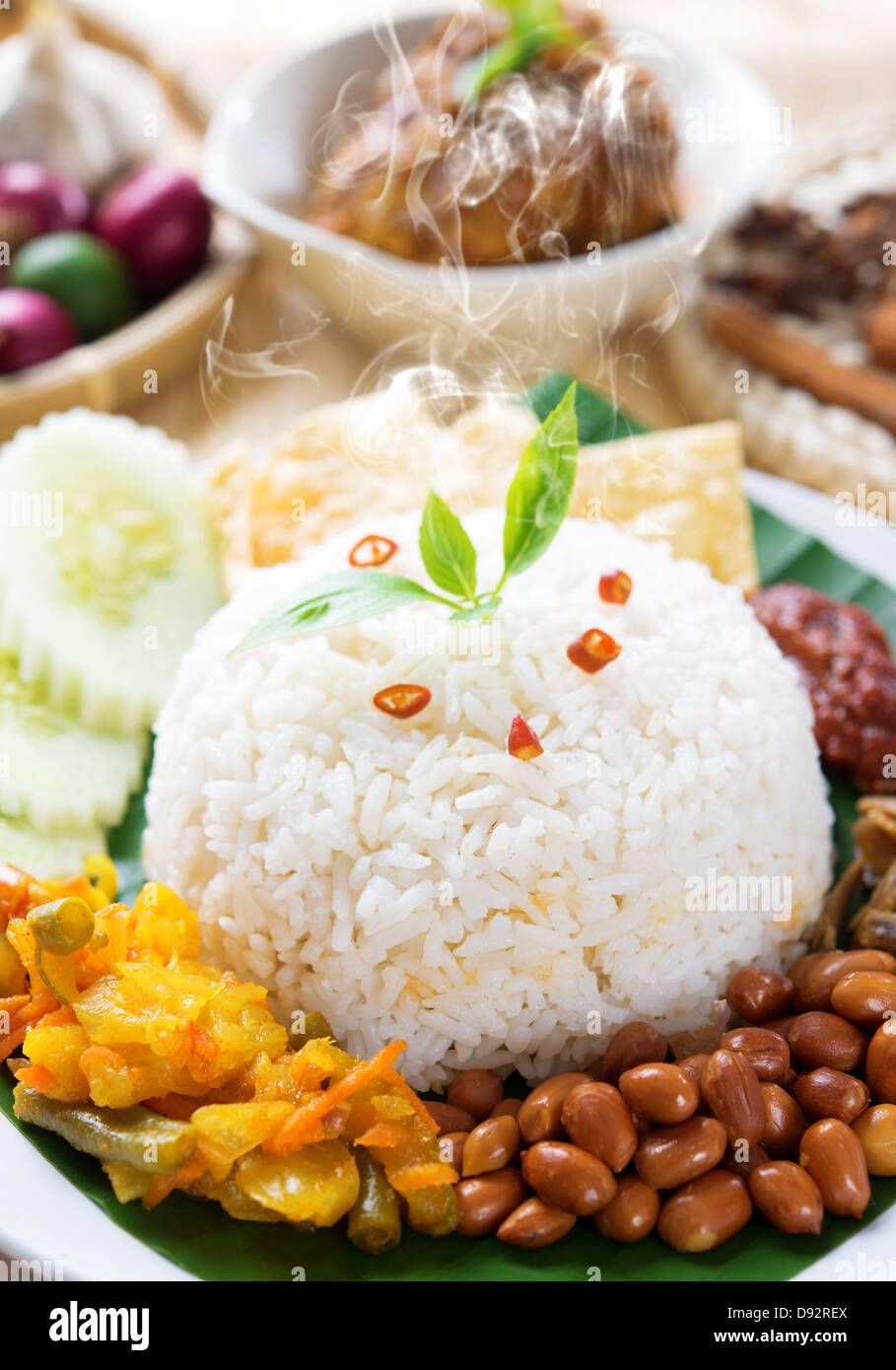 Nasi lemak traditional malaysia spicy rice dish, fresh cooked with hot steam. Served with belacan, ikan bilis, acar, peanuts and cucumber. Decoration setup, malaysian cuisine. Stock Photo