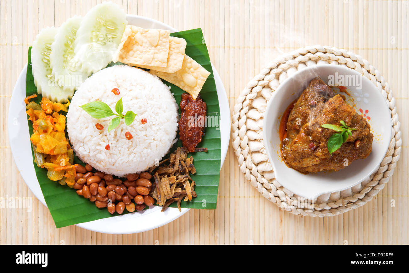 Nasi lemak is traditional malaysia spicy rice dish, fresh cooked with hot steam. Served with belacan, ikan bilis, acar, peanuts and cucumber. Decoration setup, malaysian cuisine. Stock Photo