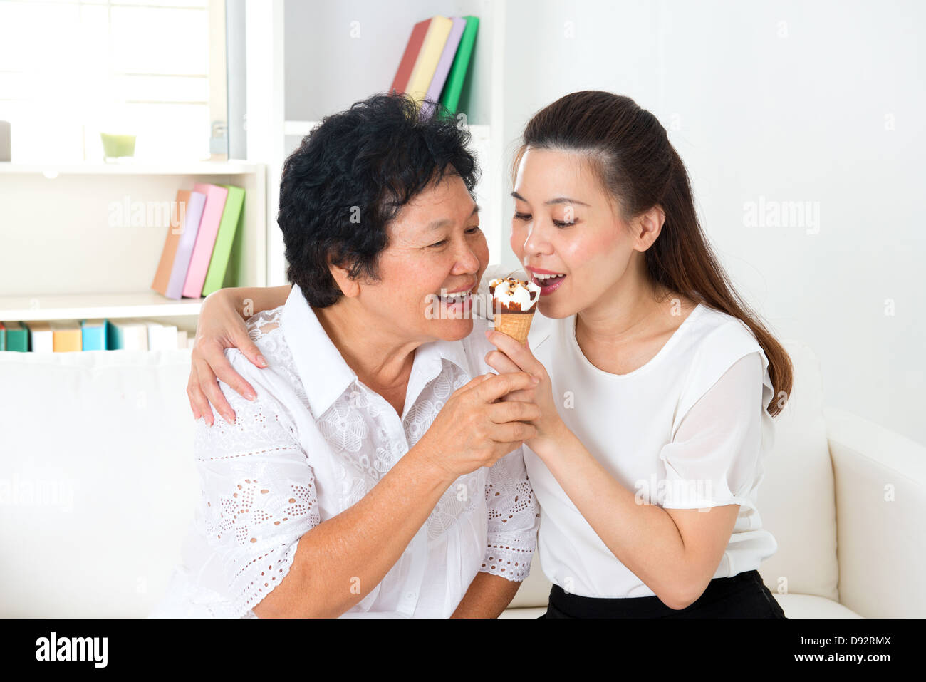 Sharing food. Happy Asian family sharing an ice cream at home. Beautiful senior mother and adult daughter eating dessert together. Stock Photo