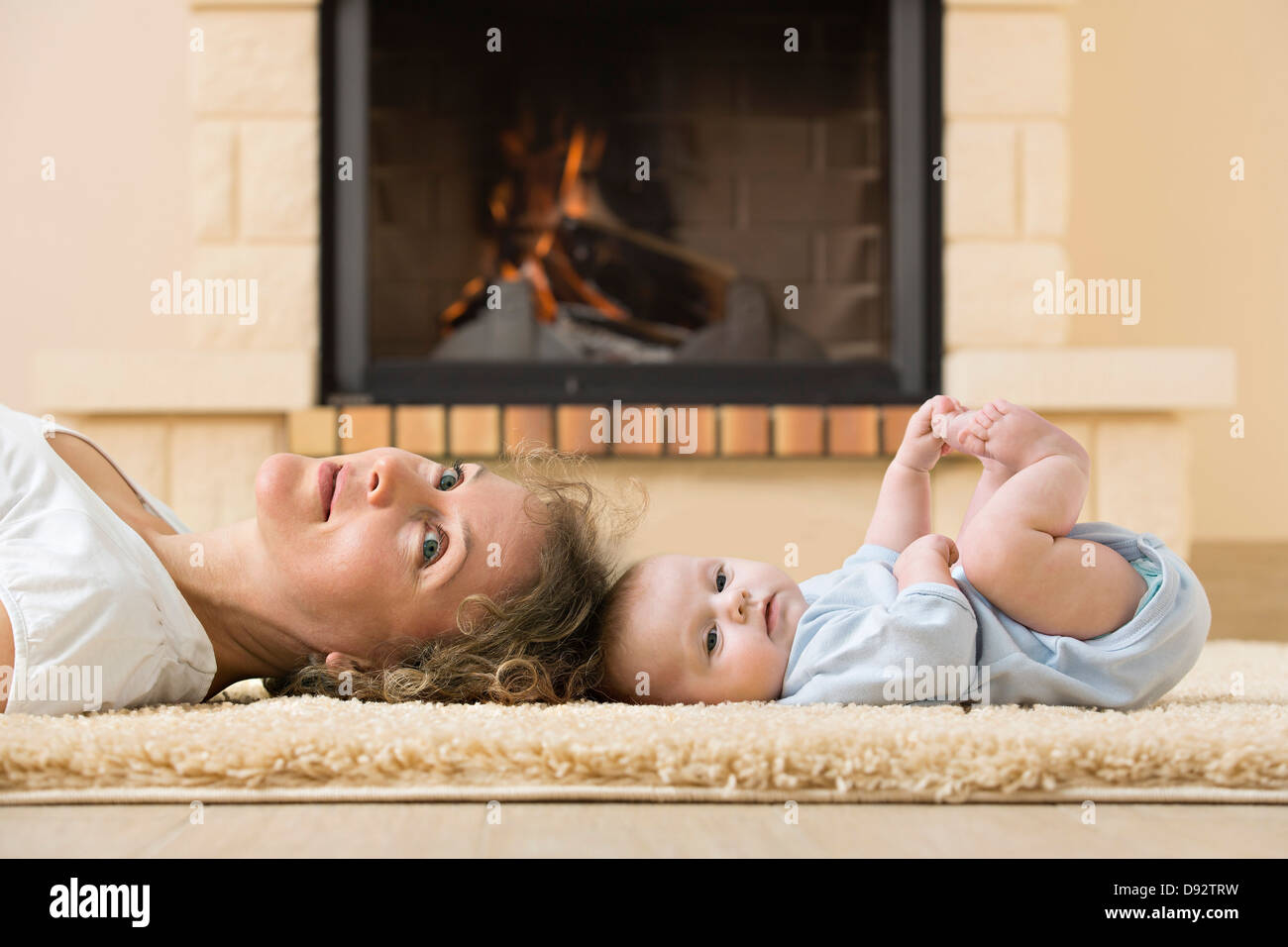 Mother and daughter lying head to head on carpet in front of fire Stock Photo