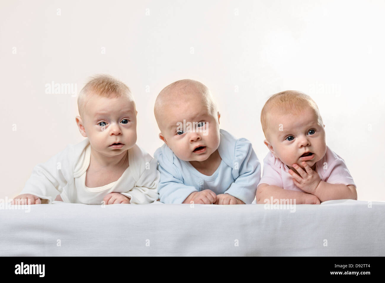 Three babies in a row pulling funny faces Stock Photo