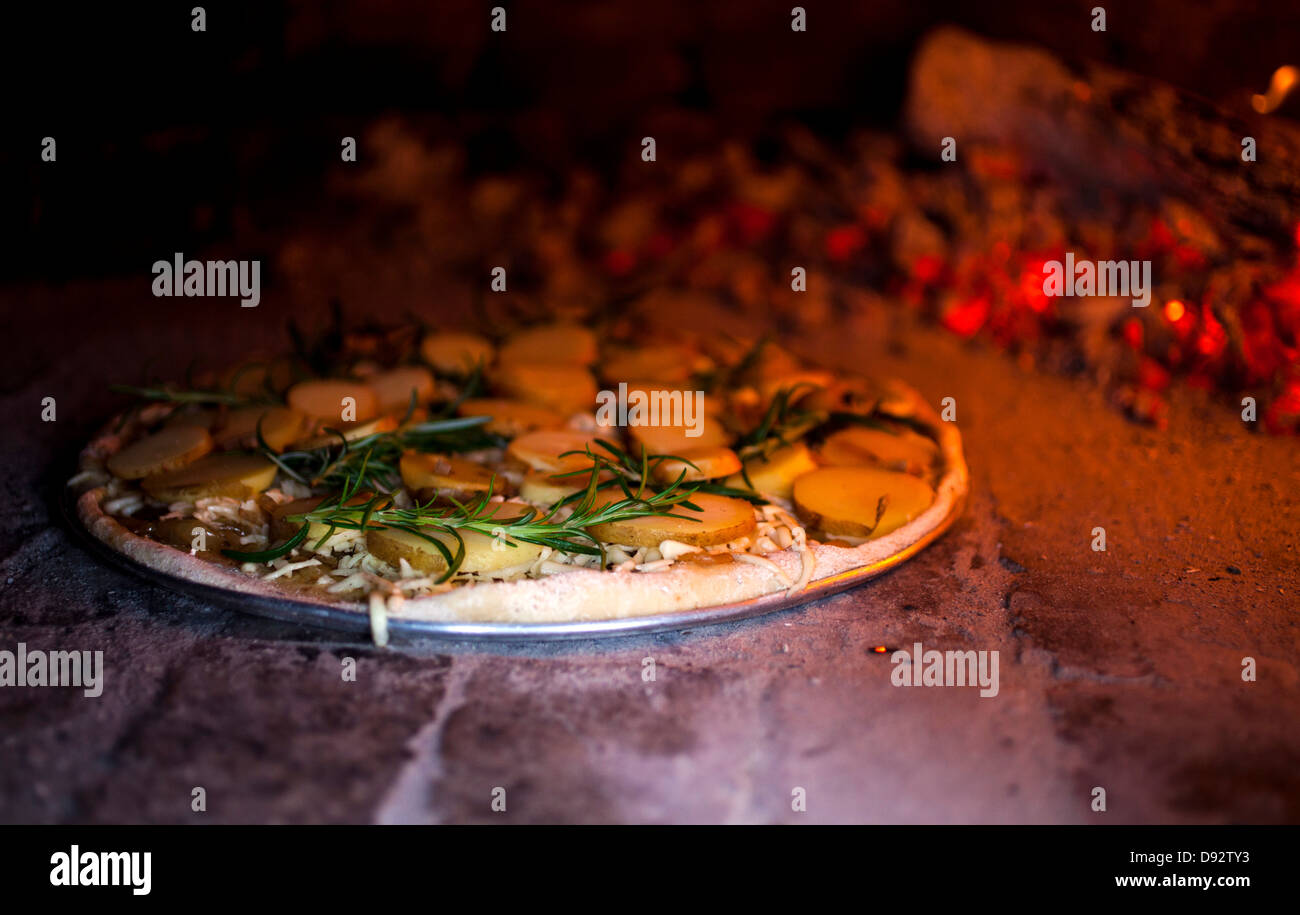 A rosemary and potato pizza baking in a brick pizza oven Stock Photo