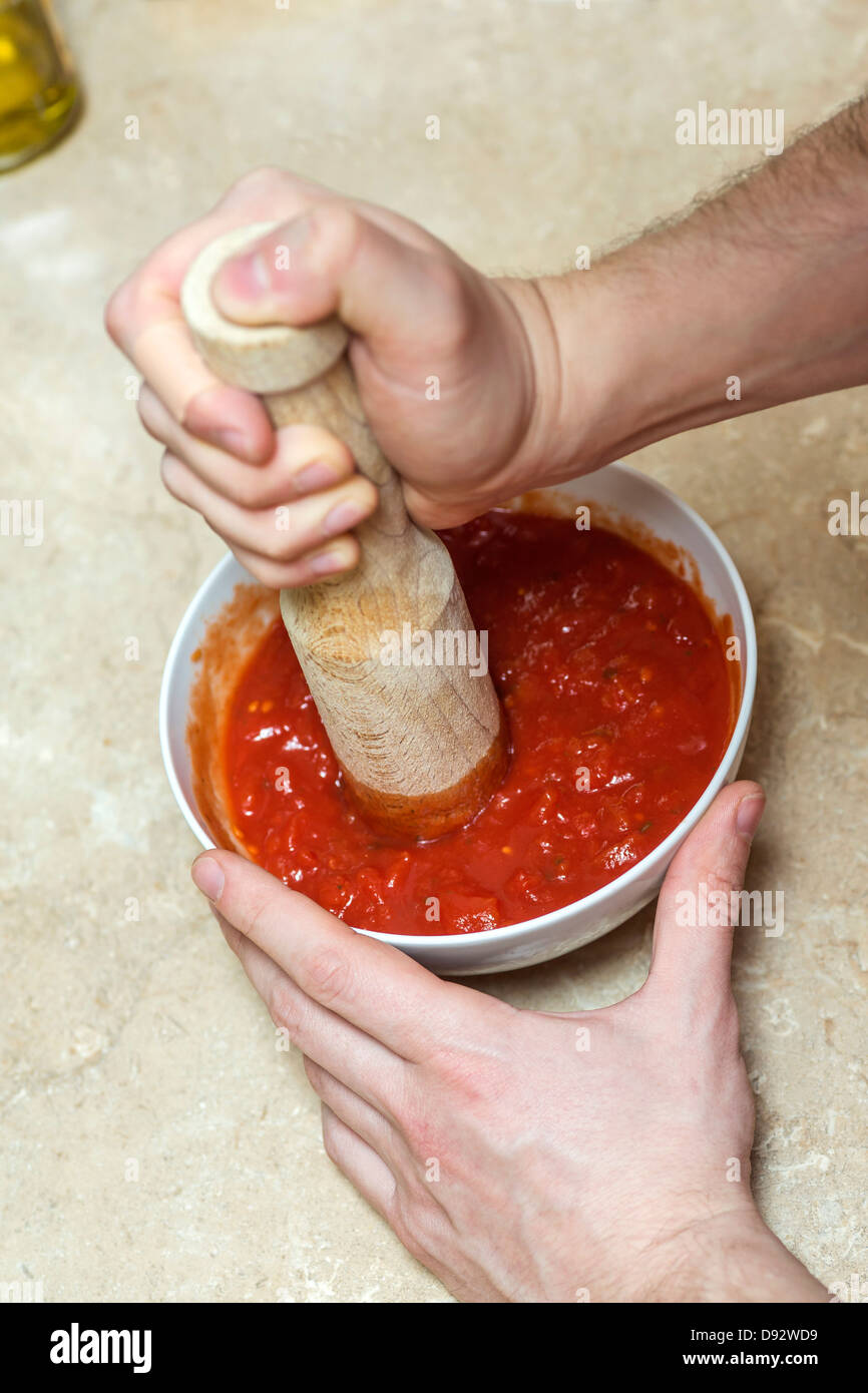 Man using wooden pestle to mix tomato sauce Stock Photo
