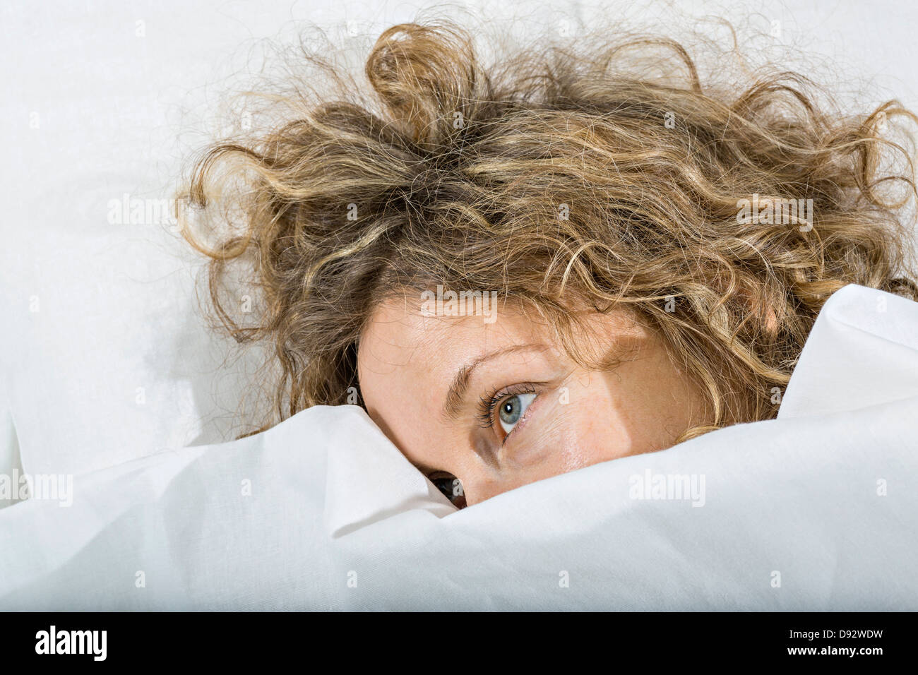 Daydreaming woman in bed under white blanket Stock Photo