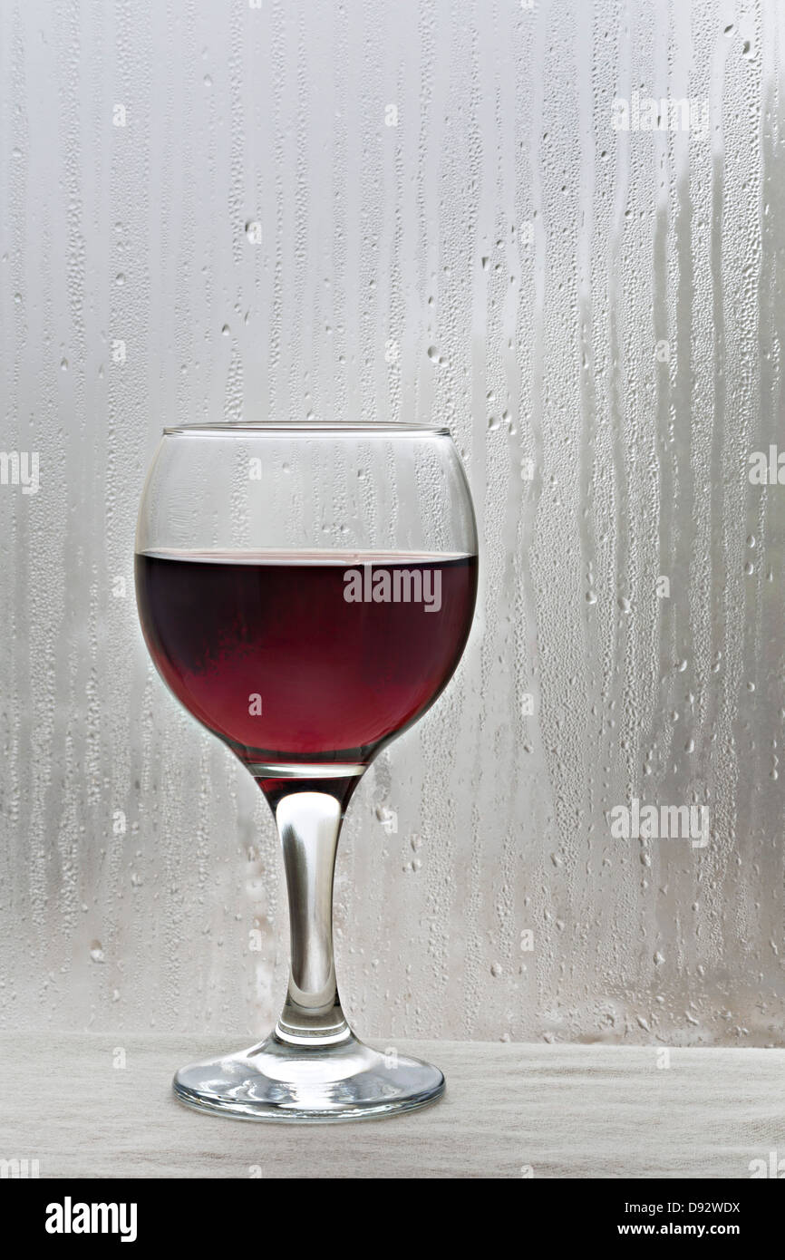 Glass of red wine by rain covered window Stock Photo