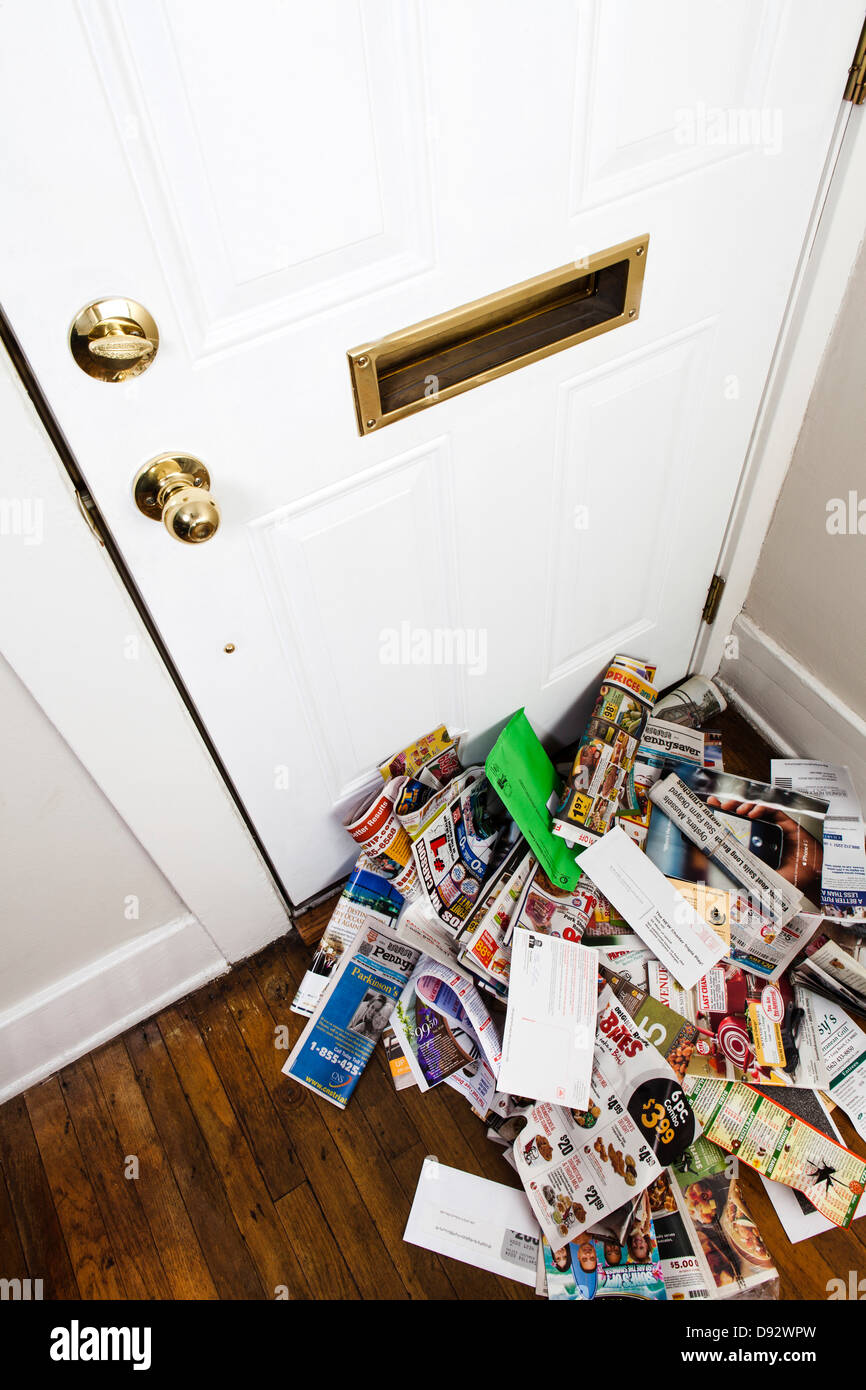 A heap of mail and newspapers under a mail slot in a home entrance hall Stock Photo