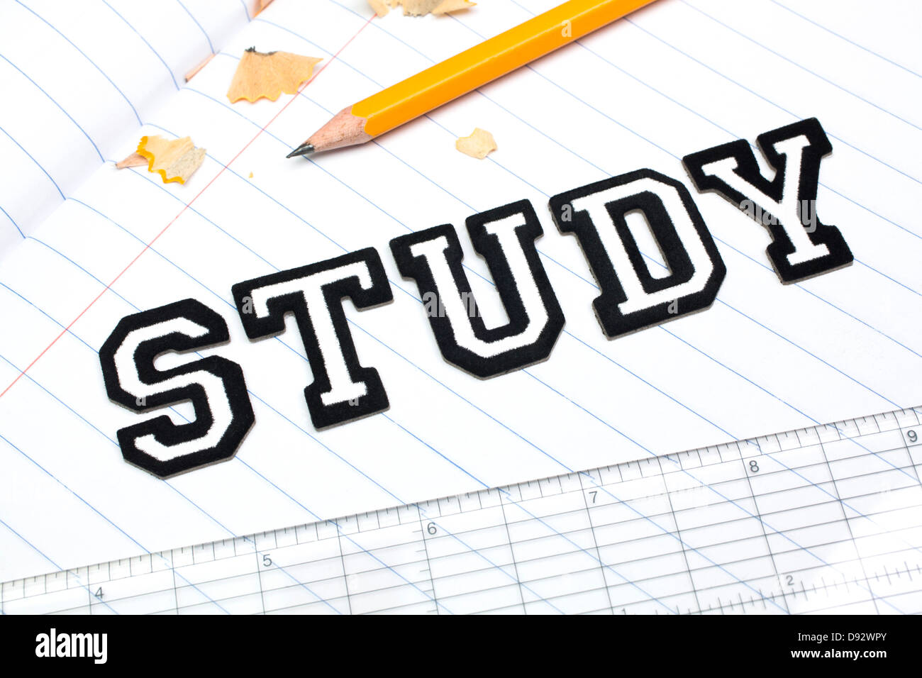Varsity font stickers spelling out Study atop a lined paper notebook with ruler and pencil Stock Photo