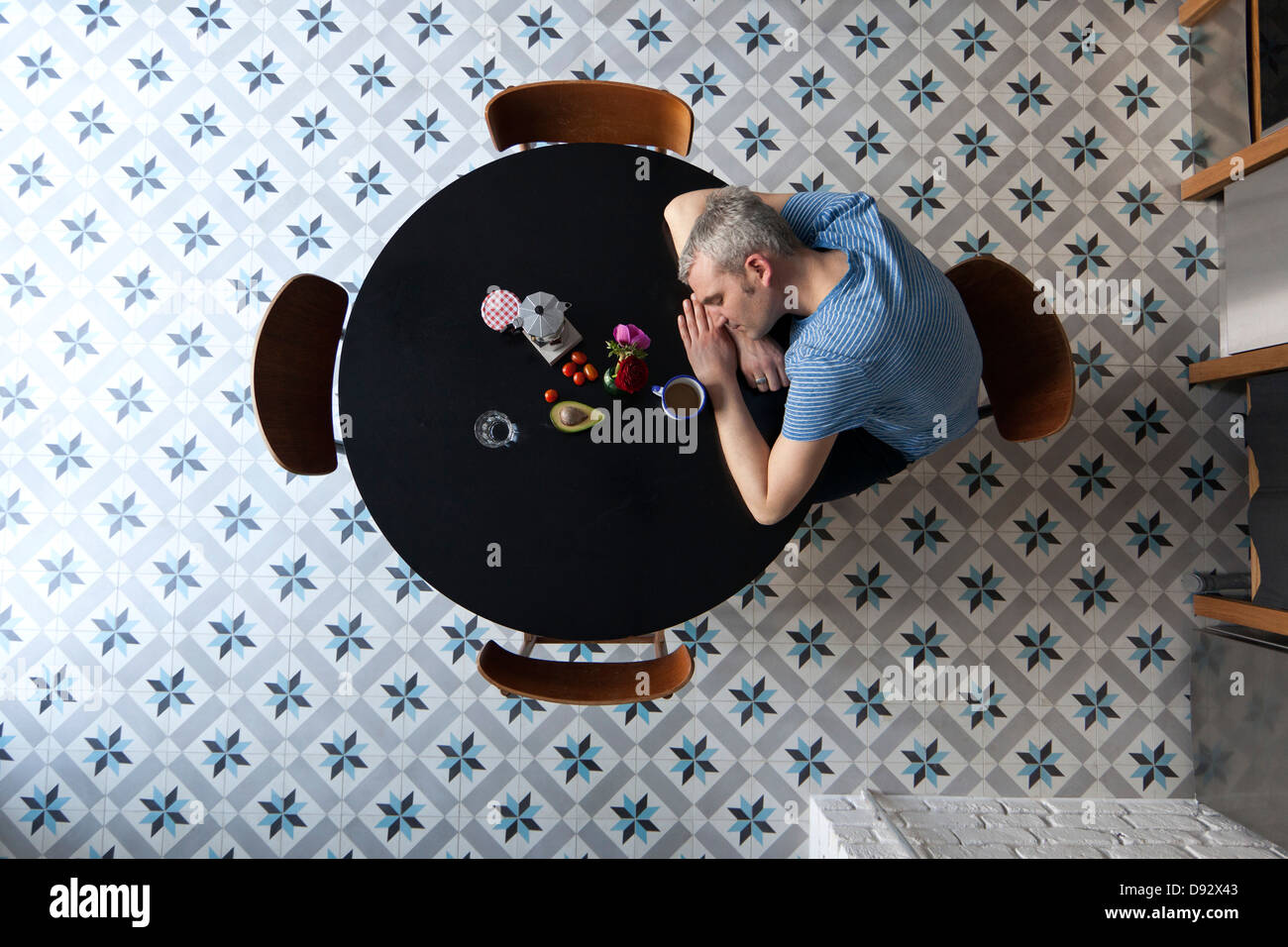 A tired man with his head resting on his arms sitting at a table, directly above Stock Photo