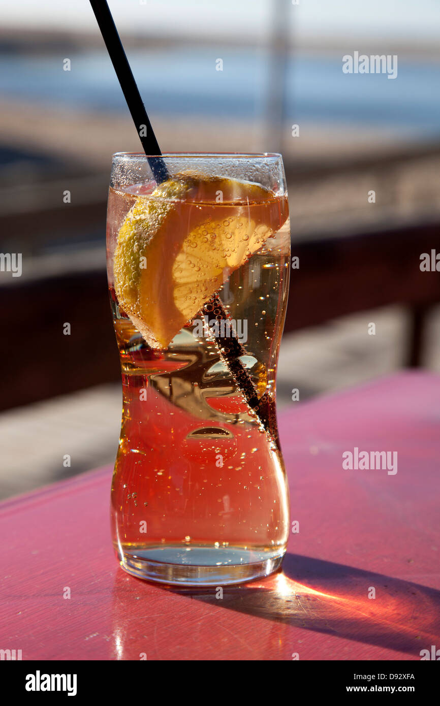 A glass of carbonated liquid with a slice of lemon and straw on a sunny day Stock Photo