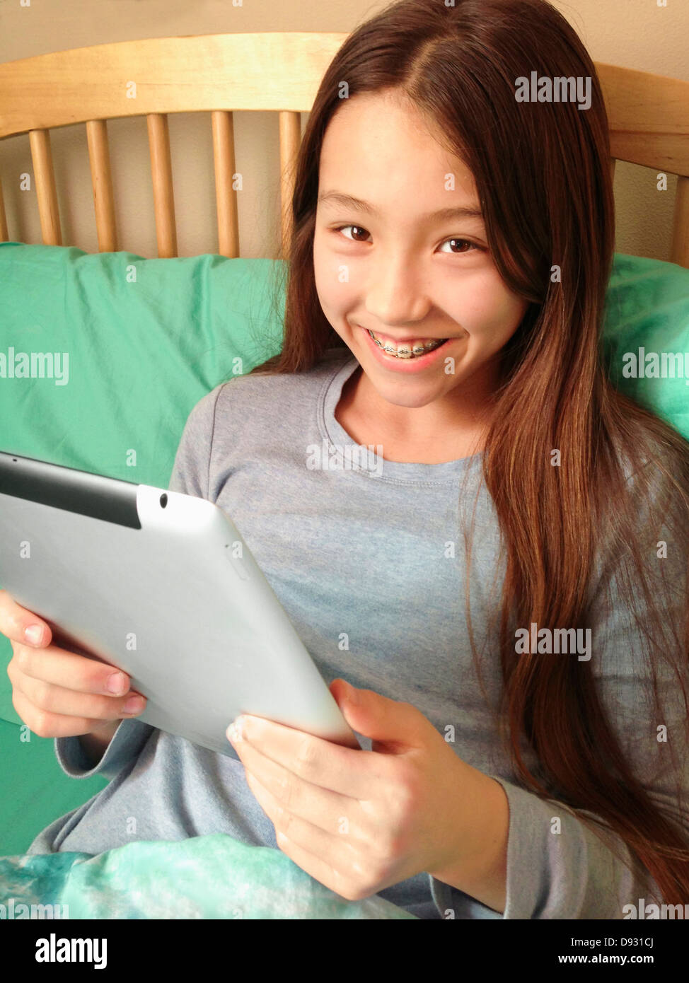 Mixed race girl using tablet computer on bed - Smartphone Captured Stock Image