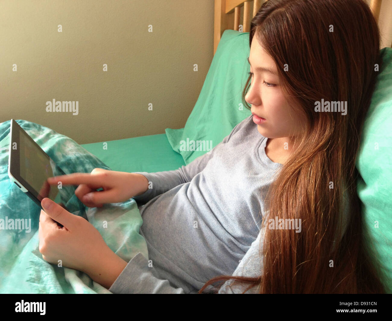 Mixed race girl using tablet computer on bed - Smartphone Captured Stock Image