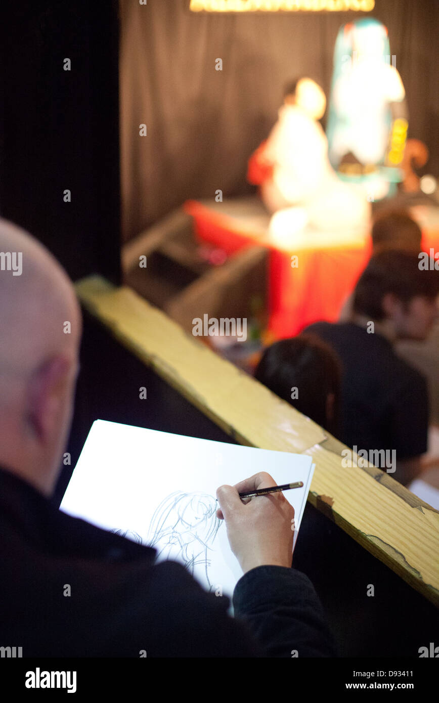 An artist sketches a young Japanese woman and cosplay anime performers onstage in anime / manga style Stock Photo