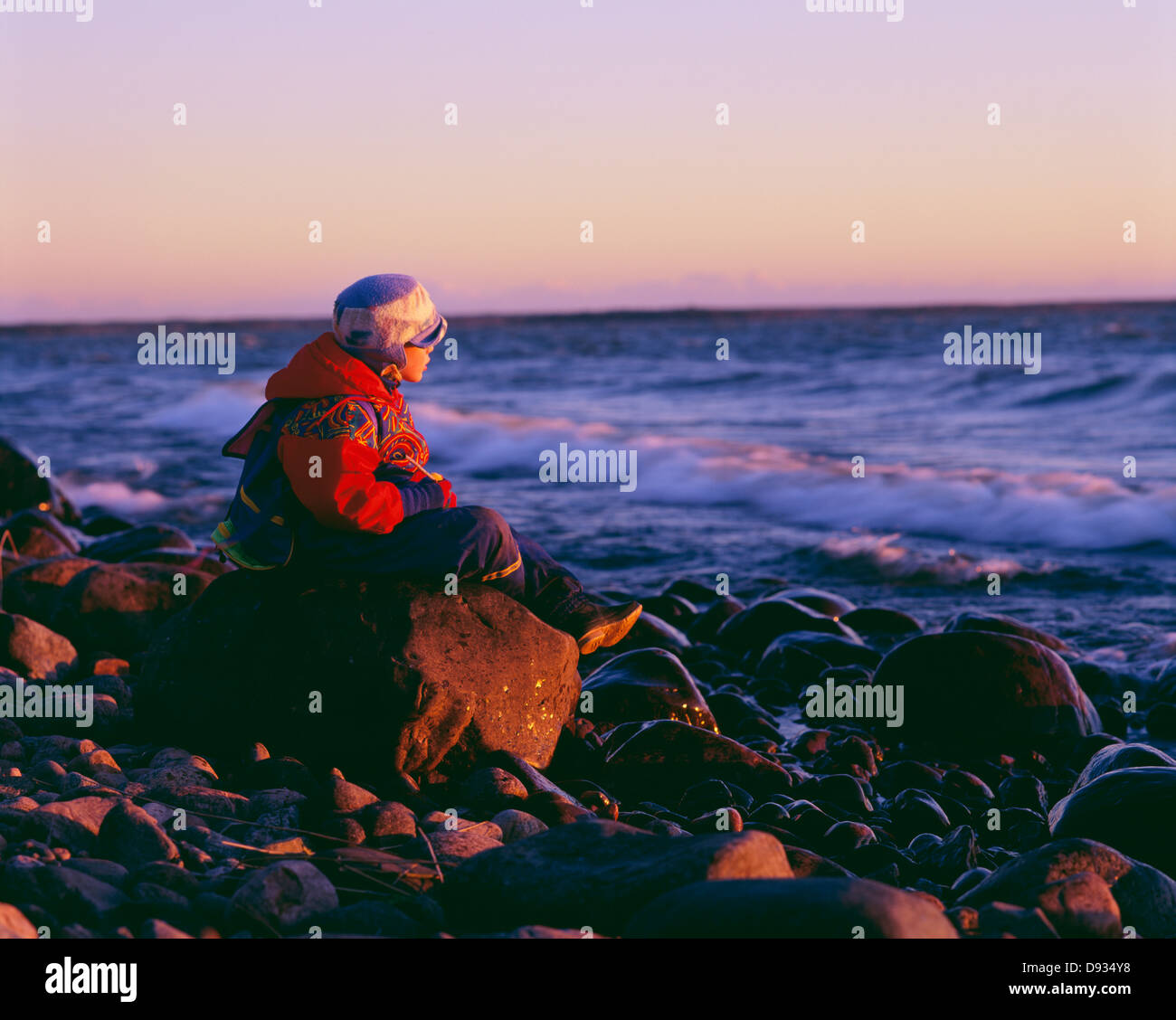 Boy sitting on rocky beach Stock Photo Alamy