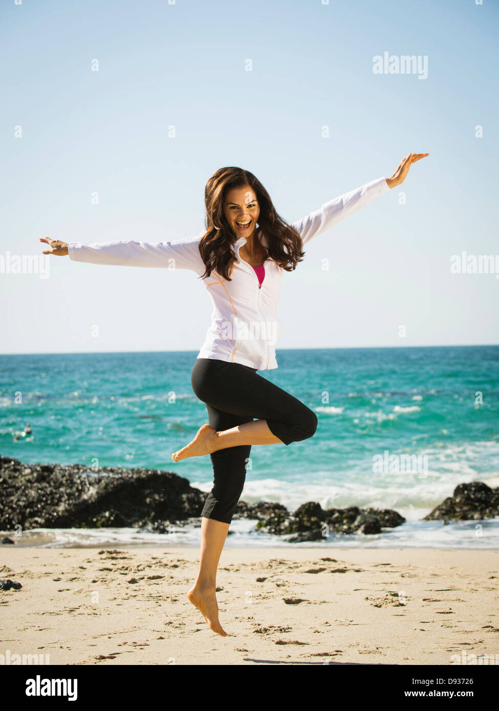 Mixed race woman jumping for joy on beach Stock Photo
