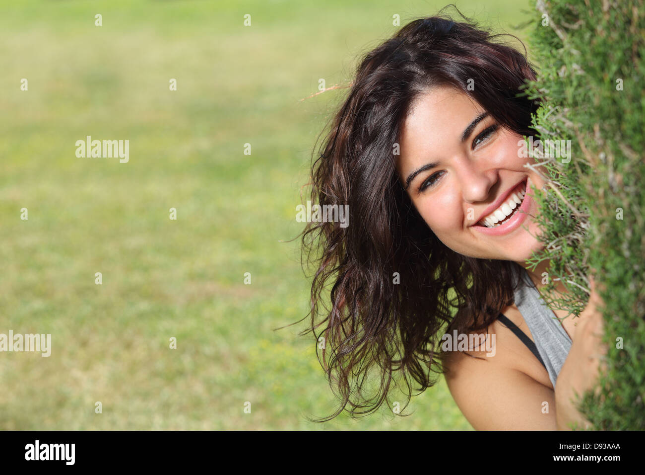 Beautiful woman peeking through a tree and smiling with a green grass background Stock Photo