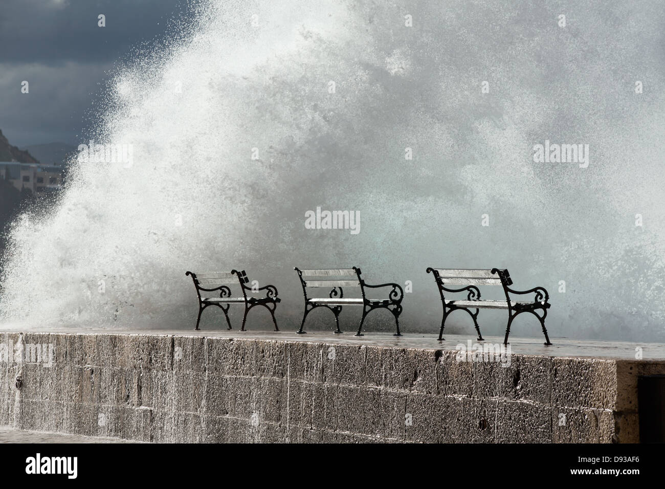 Benches with a wall of spray on a jetty wall Stock Photo