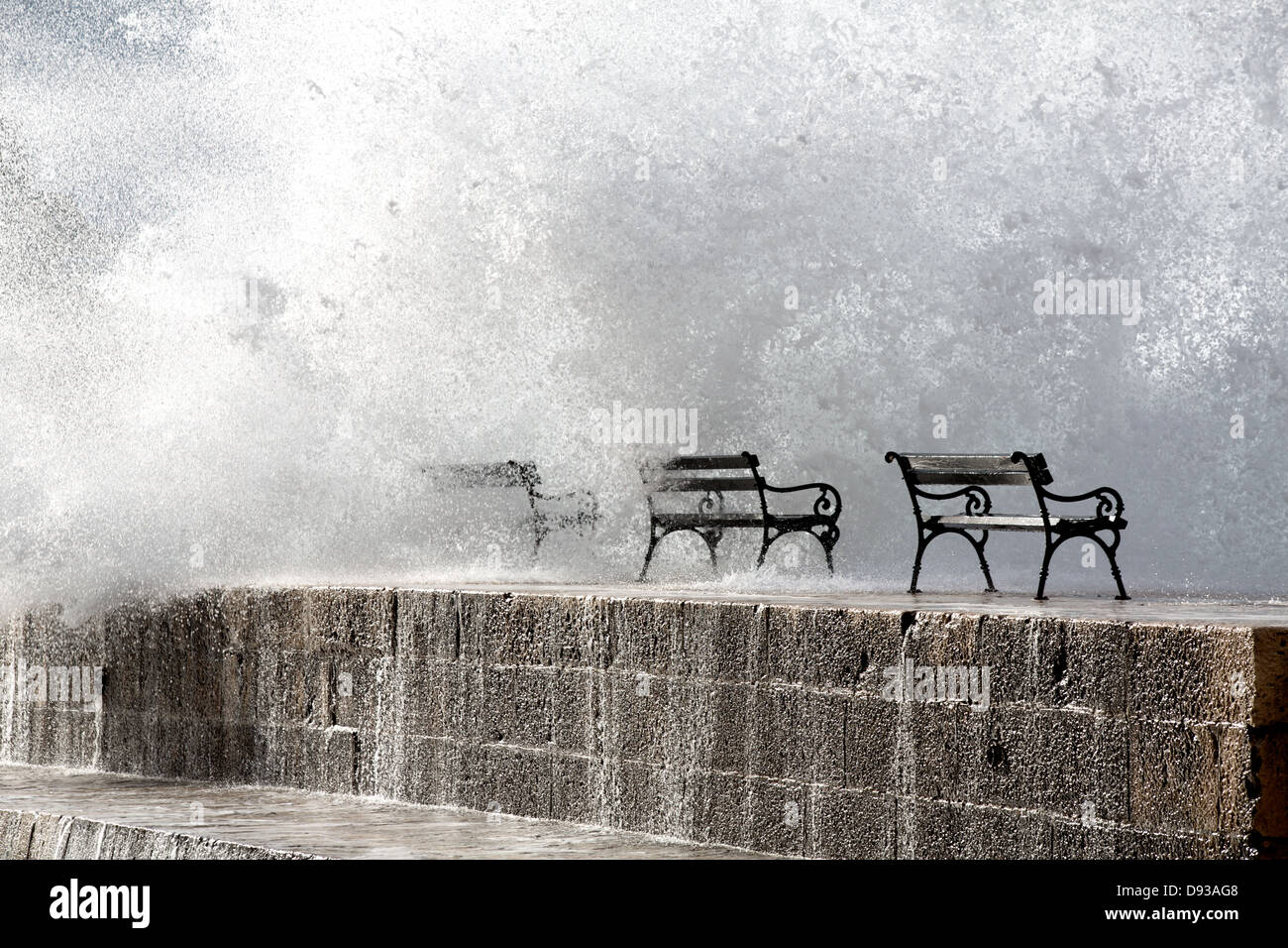 Benches with a wall of spray on a jetty wall Stock Photo