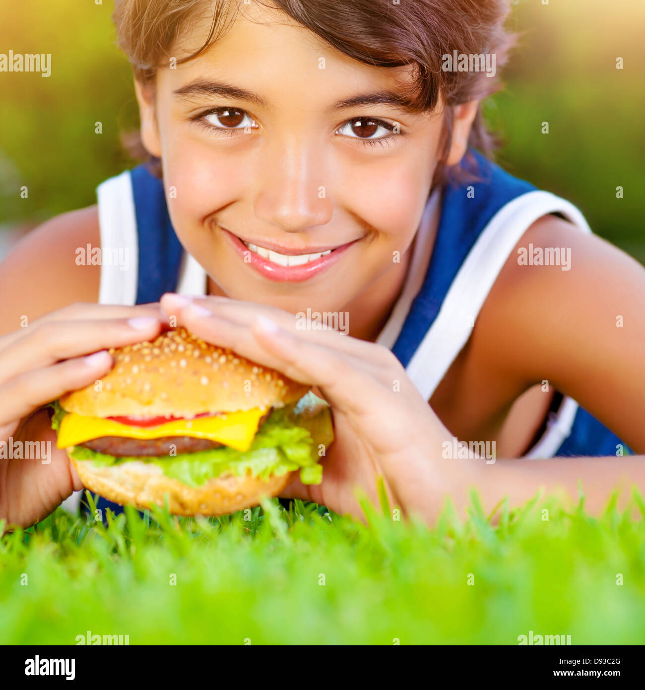 Closeup on cute boy lying down on green grass and eat delicious