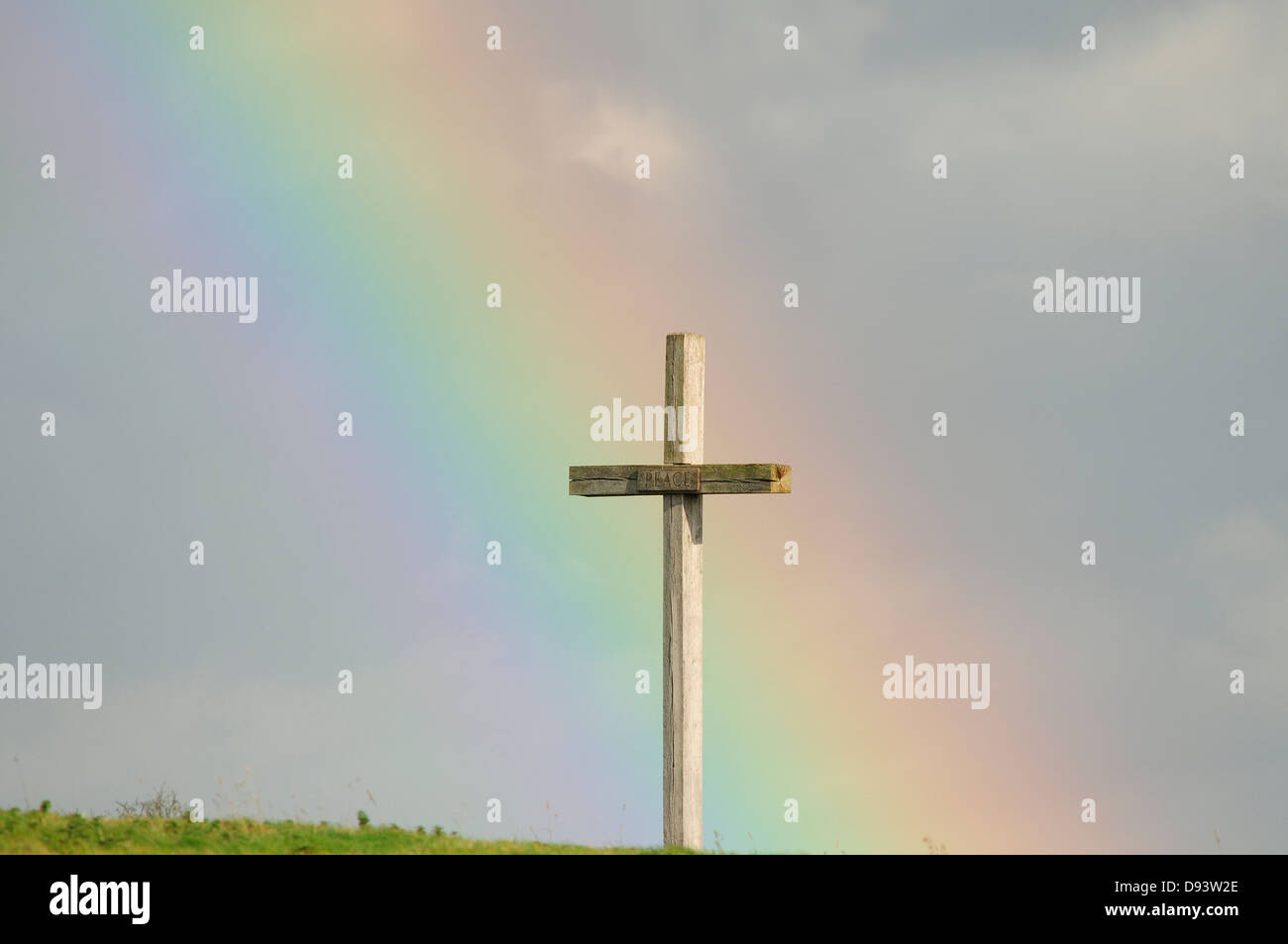 Large wooden cross in a field with a rainbow in background Stock Photo