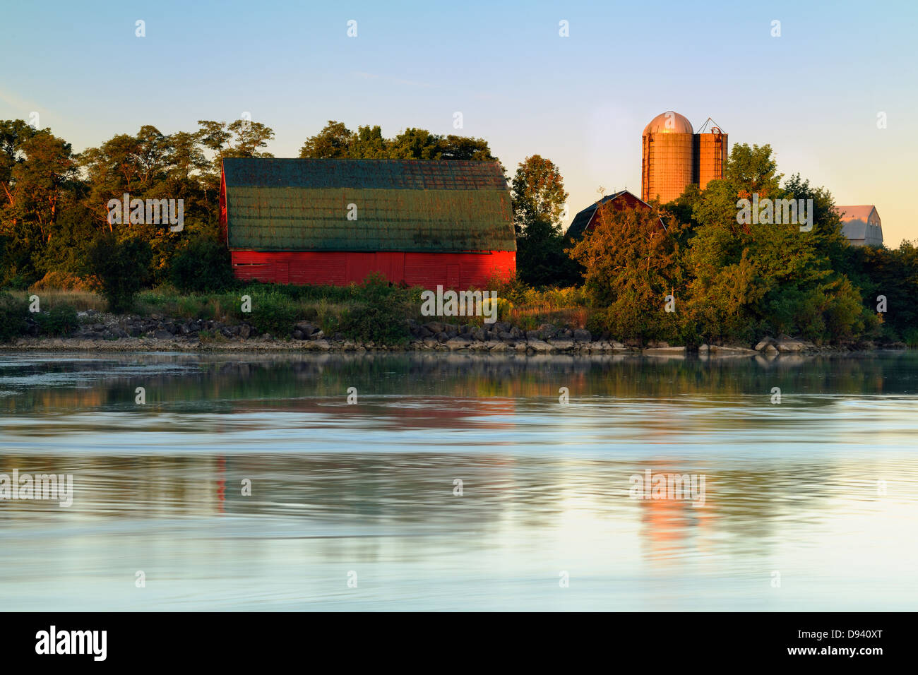 An aging red barn reflected into Gibson Lake waterway hydro controlled at dawn Thorold Ontario Canada Stock Photo