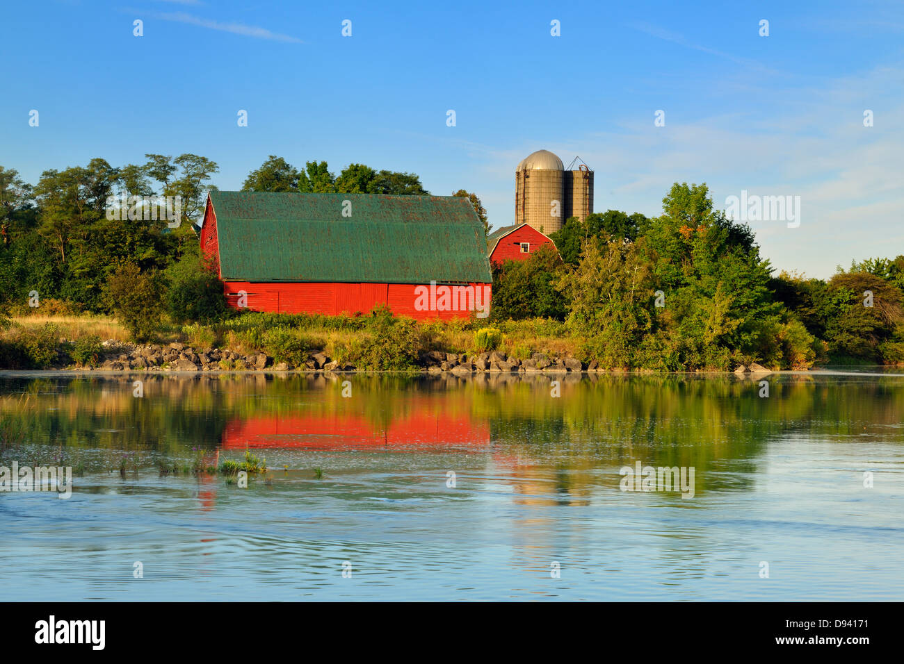 An aging red barn reflected into Gibson Lake waterway hydro controlled at dawn Thorold Ontario Canada Stock Photo