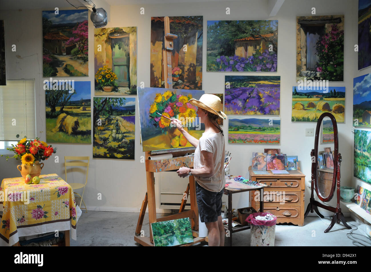Female artist painting still life subjects in studio surrounded by her artwork at studio in Laguna Beach, California Stock Photo