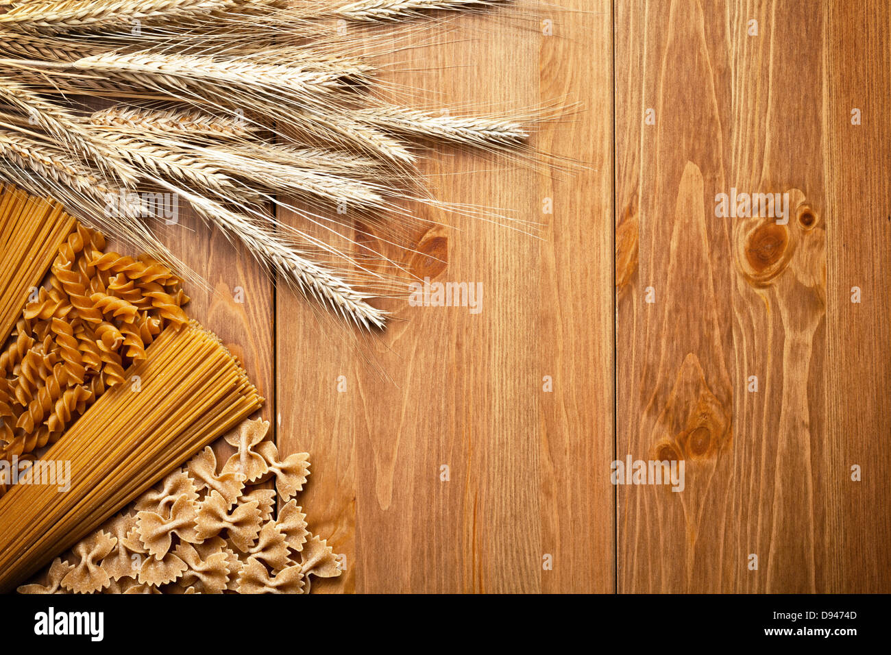 Pasta with wheat ear on wooden background. Different types of whole wheat pasta. Top view. Copy space Stock Photo