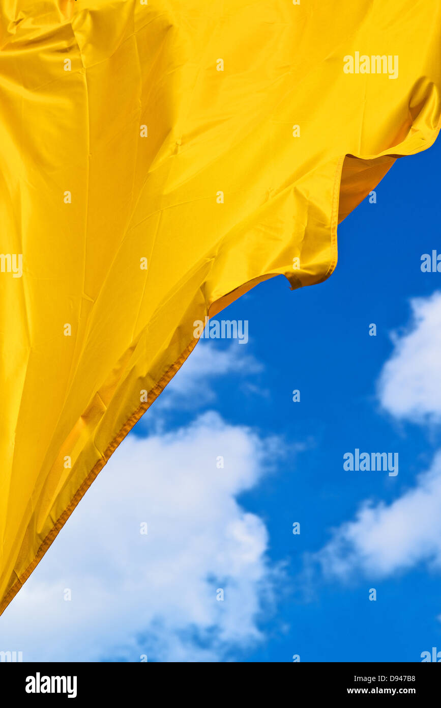 Golden waving flag against blue sky with clouds Stock Photo