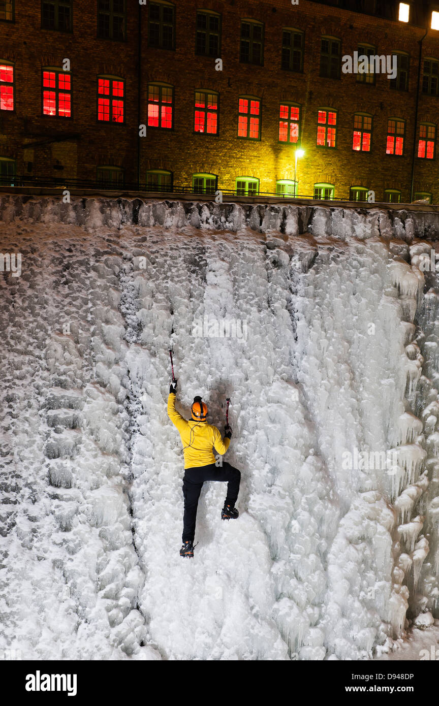 Man ice climbing up frozen waterfall in urban area Stock Photo