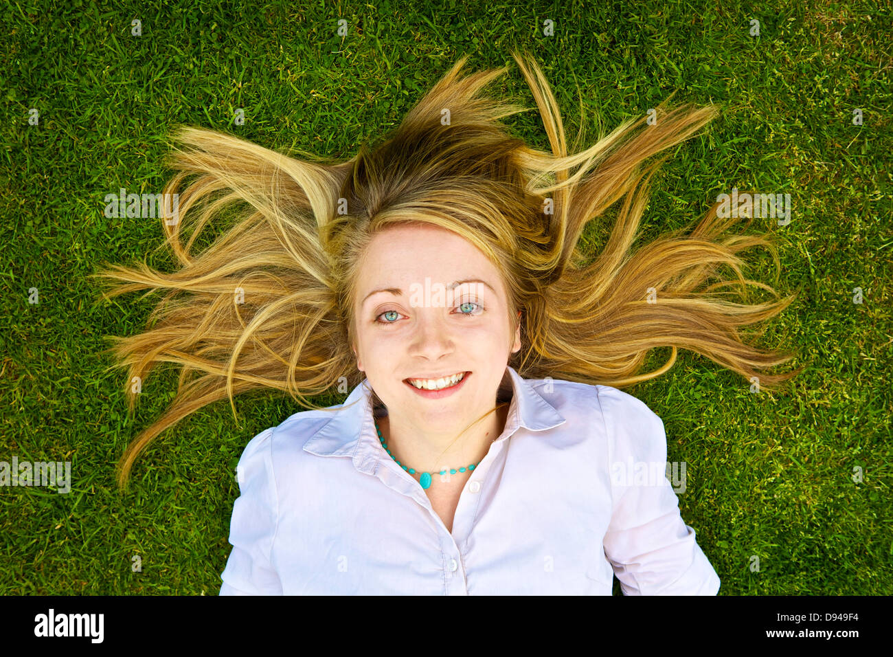 Young woman lying back on grass smiling upwards at camera Stock Photo