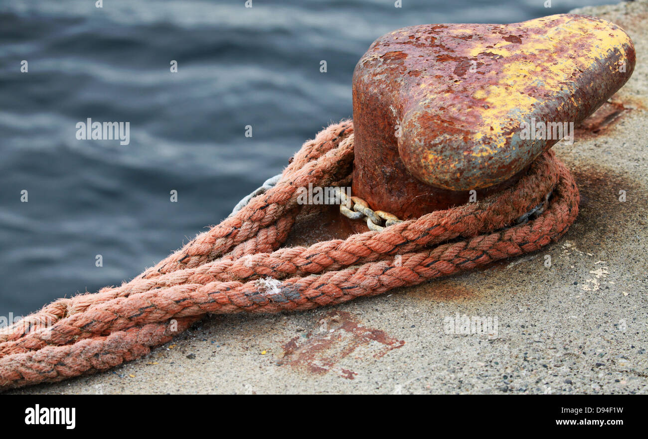 Old rusted mooring bollard with red naval rope on concrete pier Stock Photo