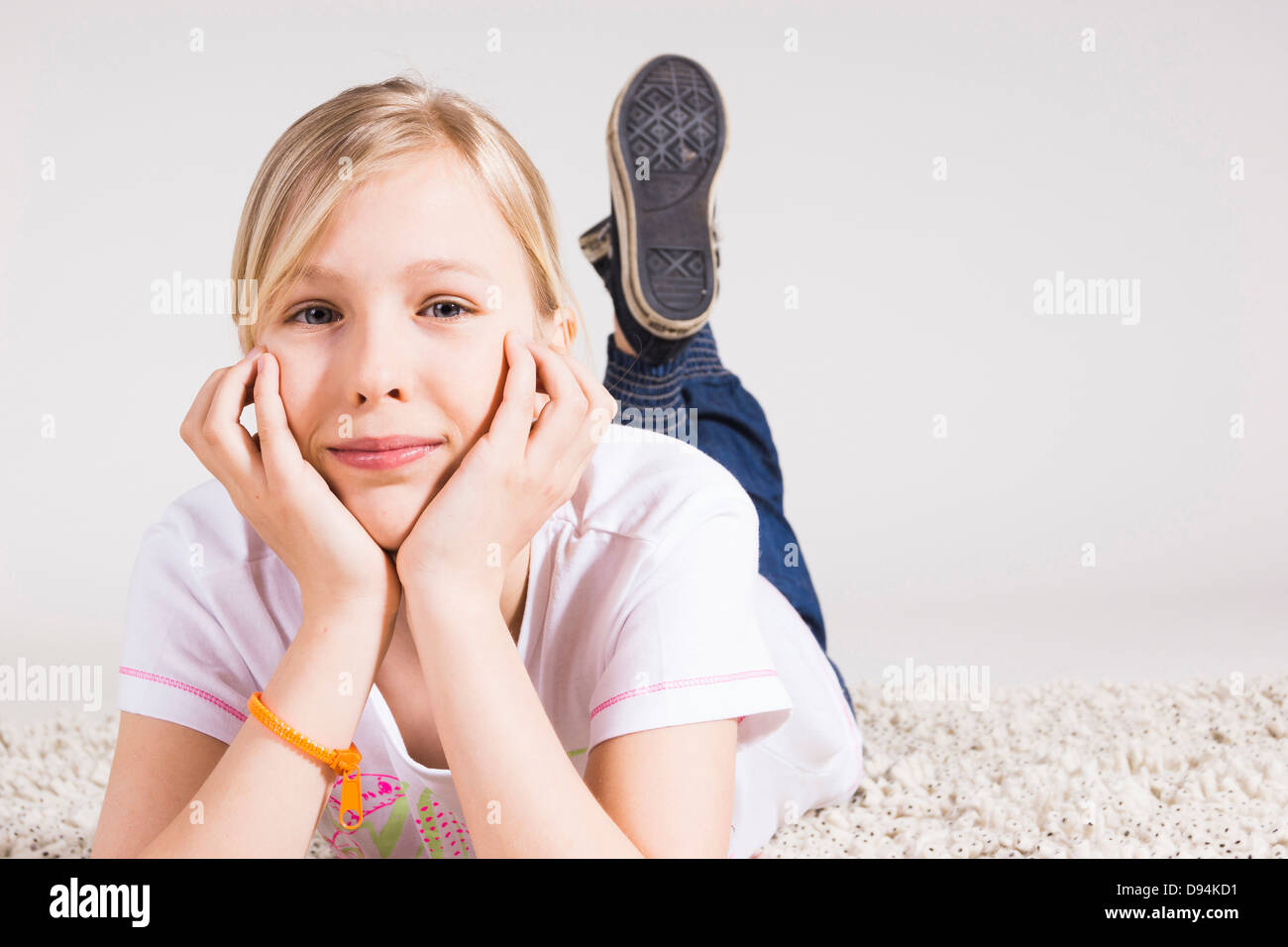 Portrait of Girl Leaning on Hands and Lying on Stomach in Studio Stock Photo